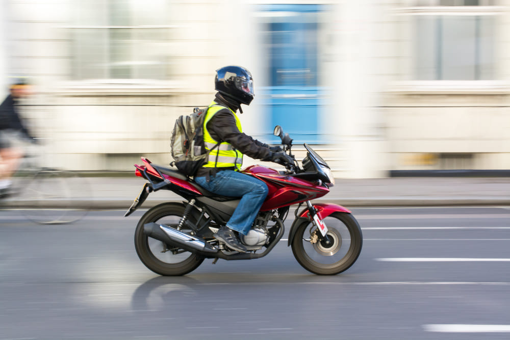 homem de mochila pilotando moto nas ruas do bairro